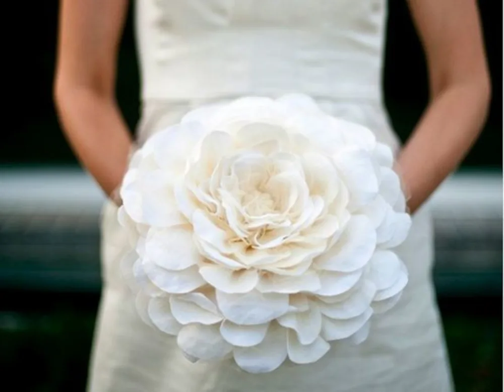Ramo de novia minimalista con una sola flor escultórica de gran tamaño sobre fondo de lino natural